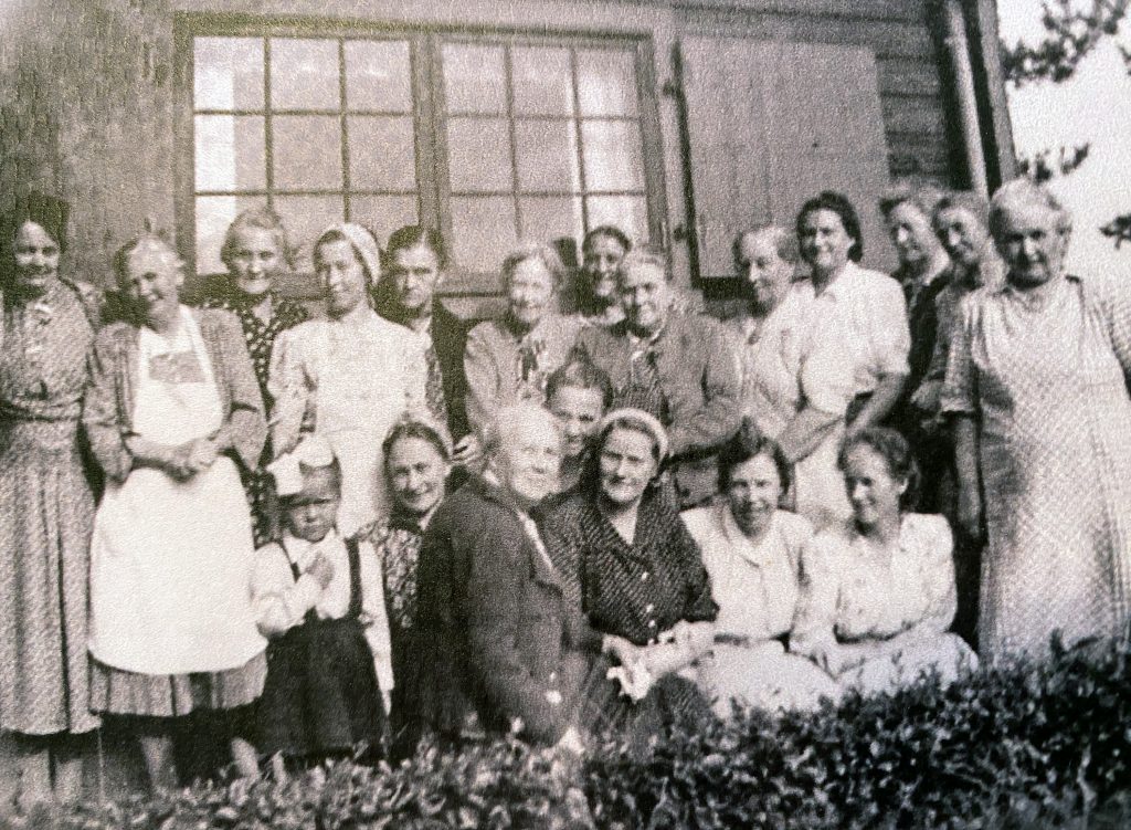 Sorthvitt bilde av kvinnene i Volla kvinneforening foran ei hytte i 1914.